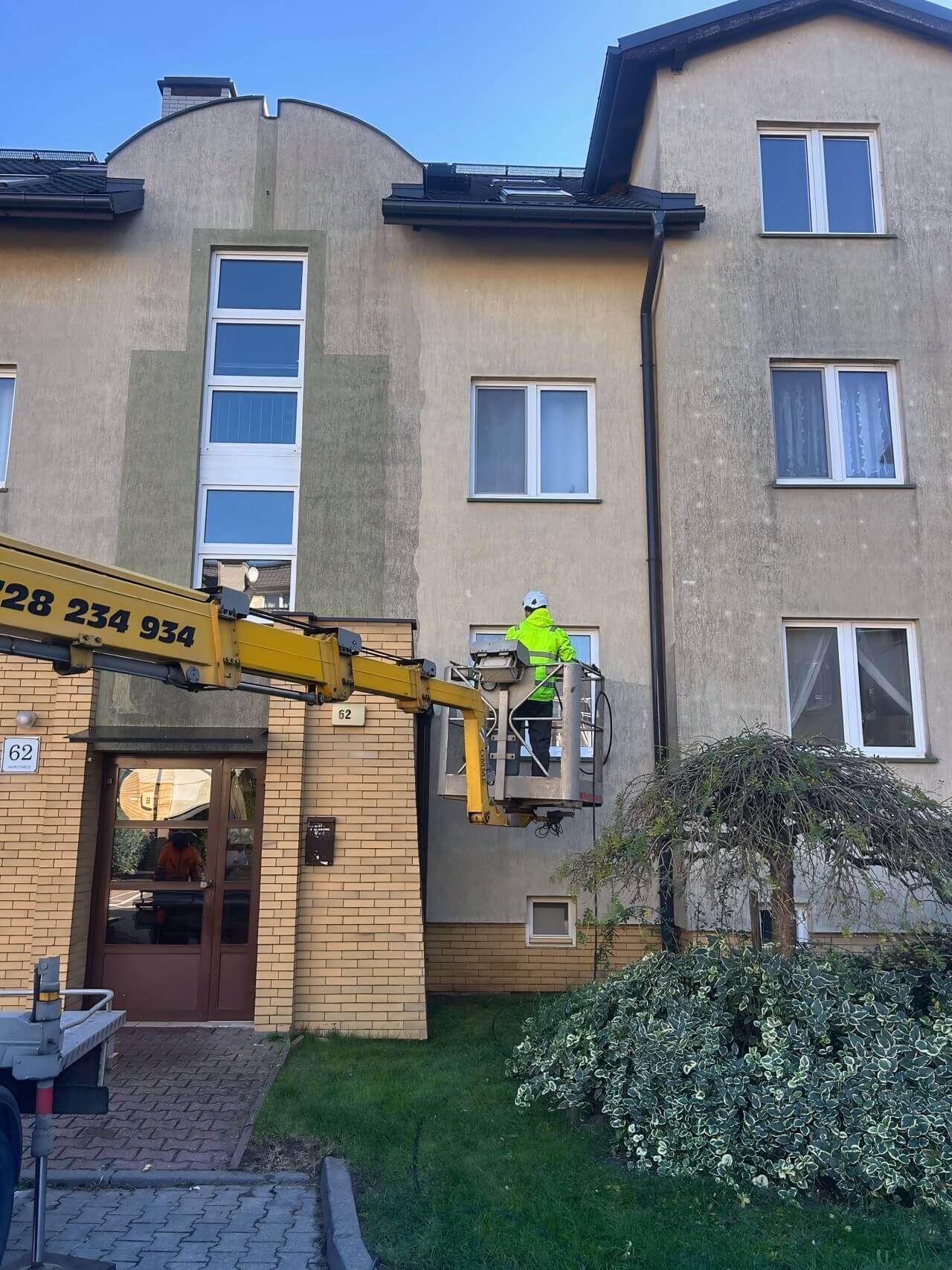 Pracownik az clean mycie elewacji bloku mieszkalnego z podnośnika koszowego