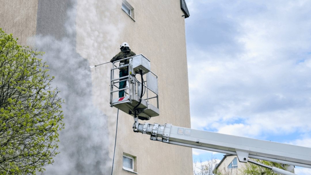 Pracownik az clean w podnośniku myjący elewację bloku metodą wysokociśnieniową